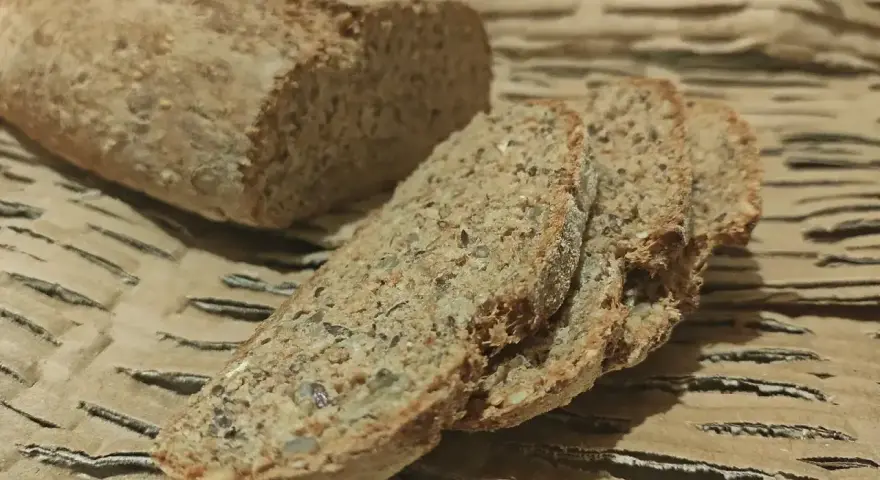 Chleb orkiszowy przepis: świeżo upieczony bochenek i kromki z ziarnami na brązowym tle.