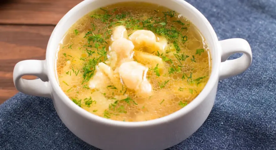 Aromaticzna zupa zacierkowa z koperkiem, podana w białej miseczce na granatowym obrusie.