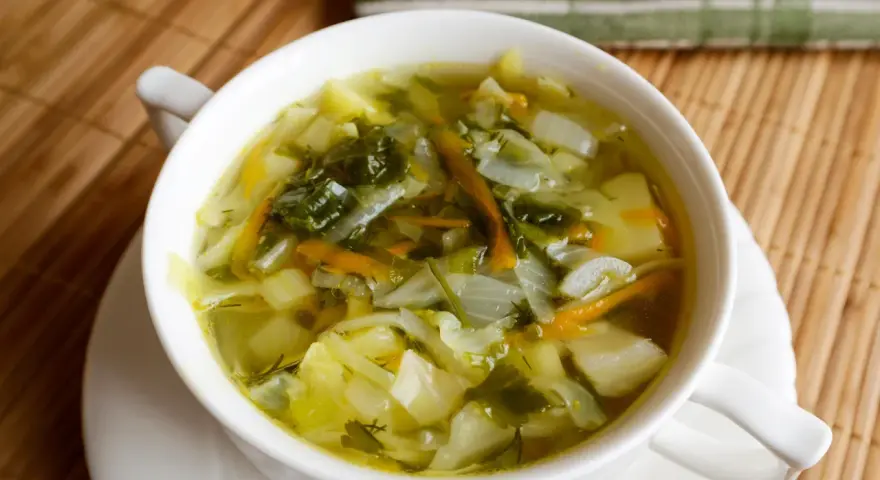 Aromaticzna zupa z młodej kapusty z ziemniakami i marchewką, podana w białej miseczce na bambusowej macie.
