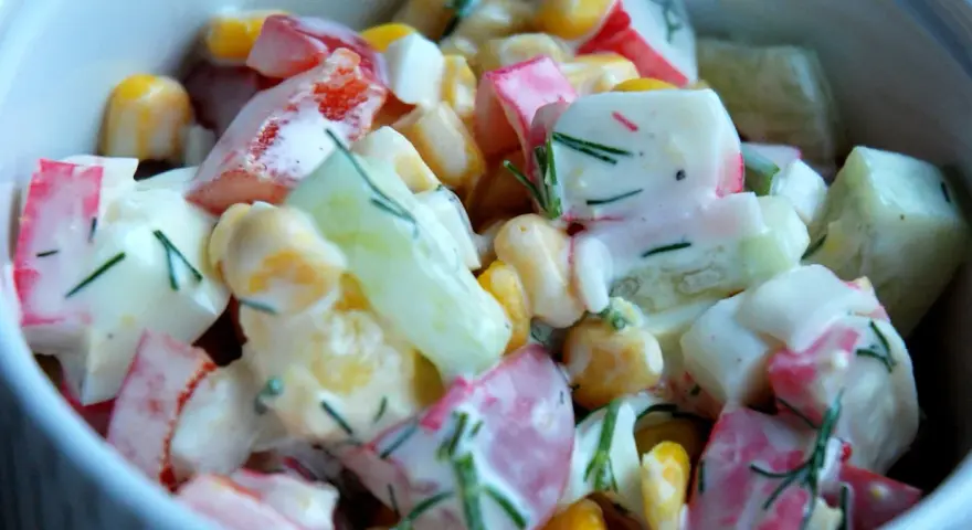 Pyszna, kremowa sałatka z surimi, kukurydzą, ogórkiem i jajkiem, posypana świeżym koperkiem. Idealna na każdą okazję, to najlepsza sałatka z surimi!