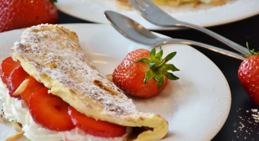 Słodki omlet z truskawkami i bitą śmietaną, posypany cukrem pudrem. Idealny przepis na omlet na słodko.