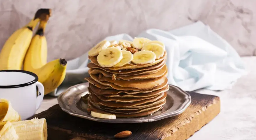 Stos naleśników z plasterkami banana i orzechami. Idealny pomysł, co zrobić z bananów na pyszne śniadanie.
