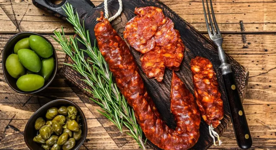 Chorizo co to? Pikantna, wędzona kiełbasa na desce z oliwkami, kaparami i rozmarynem. Idealna przekąska.