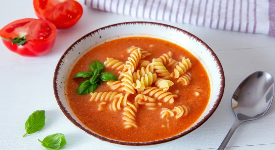 Aksamitna zupa pomidorowa z makaronem fusilli, ozdobiona bazylią. Idealne jakie przyprawy do zupy pomidorowej? Świeże pomidory obok sugerują prostotę i smak.