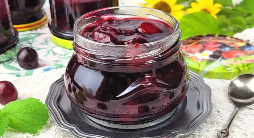 Słoiczek pełen wiśniowej frużeliny, obok świeże wiśnie i listki mięty.