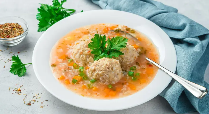 Szybka zupa na obiad z klopsikami, ryżem i warzywami, udekorowana natką pietruszki.