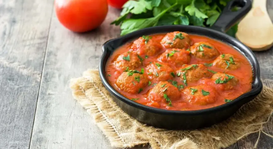 Pyszne pulpeciki w sosie pomidorowym, posypane natką pietruszki, gotowe do podania.