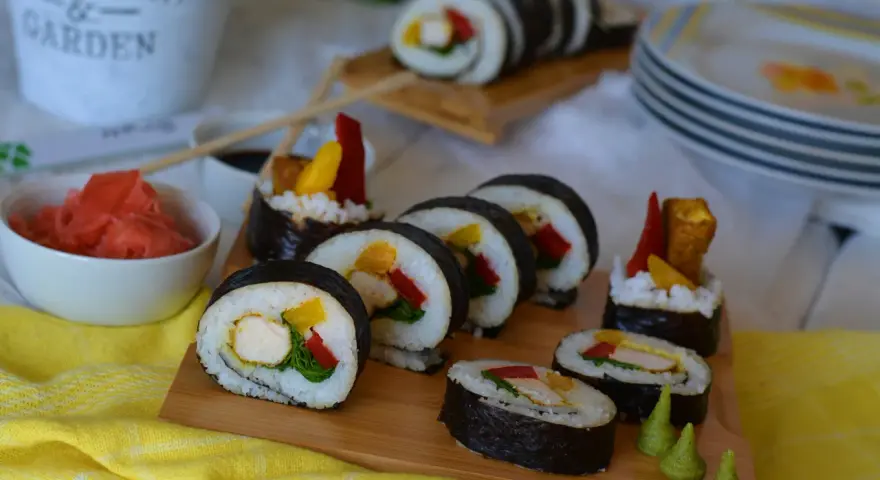 Pyszne sushi z kurczakiem, papryką i mango. Podane na desce z dodatkami: marynowanym imbirem i wasabi.