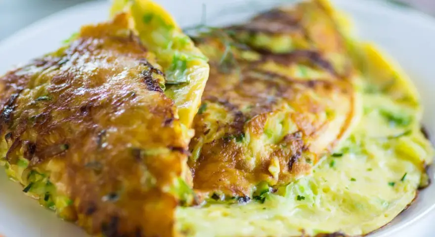 Złocisty omlet z cukinią, delikatnie zrumieniony, podany na białym talerzu.