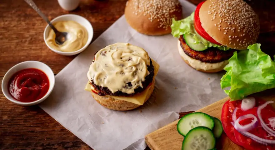 Pyszny sos do burgera, ketchup i majonez czekają na idealne kanapki. Obok świeże warzywa i bułki z sezamem.