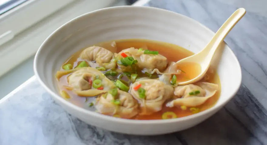 Aksamitna zupa wonton z kawałkami chili i szczypiorku, gotowa do nabrania łyżką.