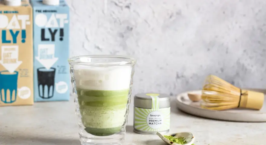 Zielony napój warstwowy w szklance, obok puszka z napisem "PREMIUM MATCHA" i bambusowa miotełka. To jest właśnie co to matcha.