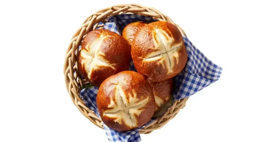 Koszyk z kilkoma bułkami bawarskimi, ułożonymi na niebiesko-białej kratkowanej ściereczce.