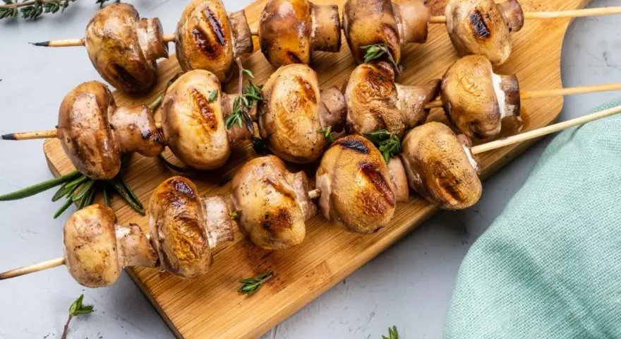 Grillowane pieczarki na drewnianej desce, przyprawione ziołami. Idealne na letnie przyjęcie.