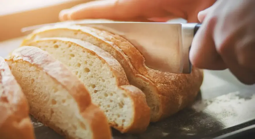 Dłoń kroi świeży chleb na kromki. Zastanawiasz się, jak odświeżyć chleb? Ten obrazek pokazuje, jak zacząć.