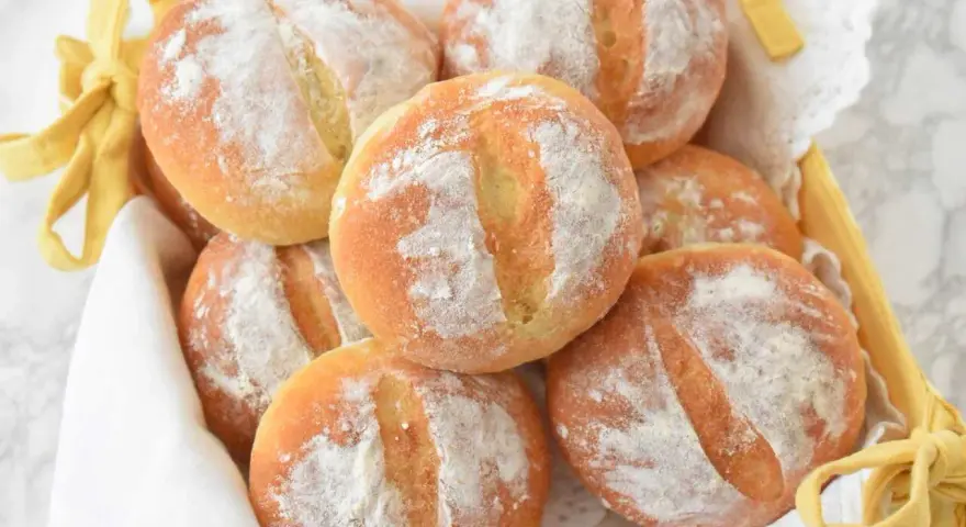 Koszyk pełen świeżych, puszystych bułek ziemniaczanych, posypanych mąką. Idealne na śniadanie.