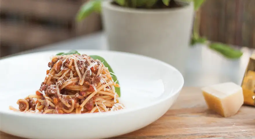 Pyszne spaghetti bolognese, przygotowane według oryginalnego przepisu, posypane parmezanem i udekorowane listkiem bazylii.