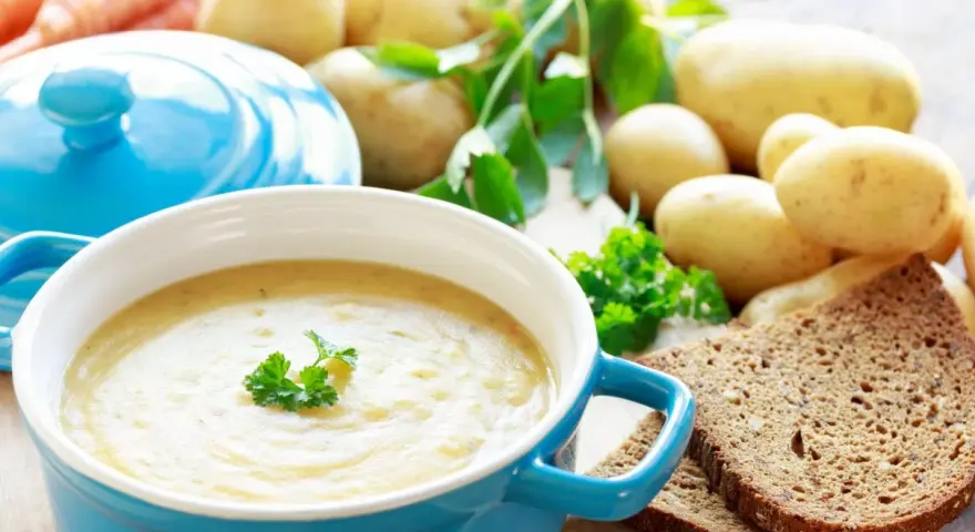 Aksamitna zupa ziemniaczana, przepis babci, z chlebem i świeżymi ziemniakami w tle.