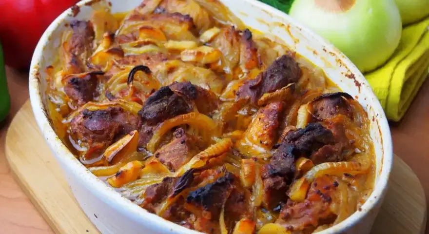 Pyszne danie z łopatki na szybko, zapiekane z cebulą w białym naczyniu. Obok papryka, cebule i koperek.