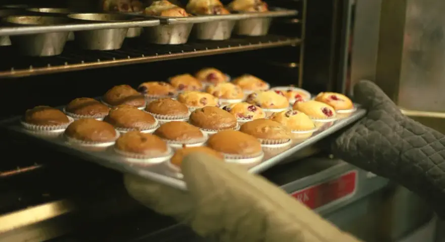 Rękawice wyjmują z piekarnika blachę z gotowymi muffinkami, które idealnie nadają się do przepisu na wilgotne i puszyste muffinki.