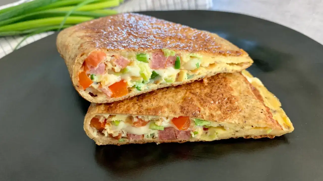 Keto tortilla przepis: złocista tortilla z jajkiem, warzywami i wędliną, pokrojona na pół, prezentuje sycące nadzienie.