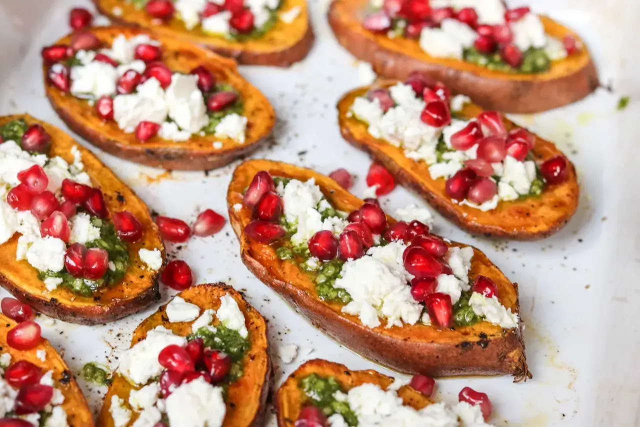 Pieczone bataty z piekarnika, udekorowane fetą, pestkami granatu i zielonym pesto. Pyszna przekąska!