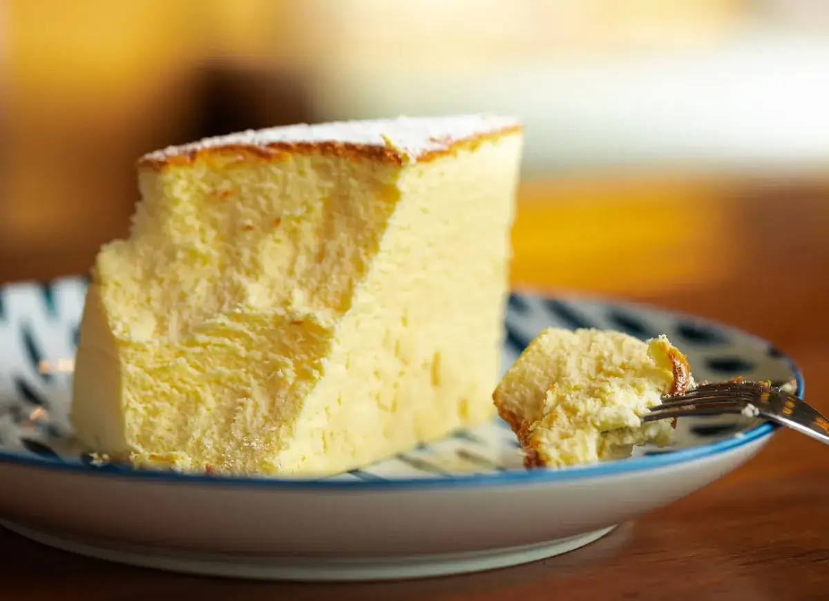Puszyste ciasto z serkiem mascarpone pieczone, lekko oprószone cukrem pudrem. Kawałek na talerzyku, widelczyk już zaczął degustację.