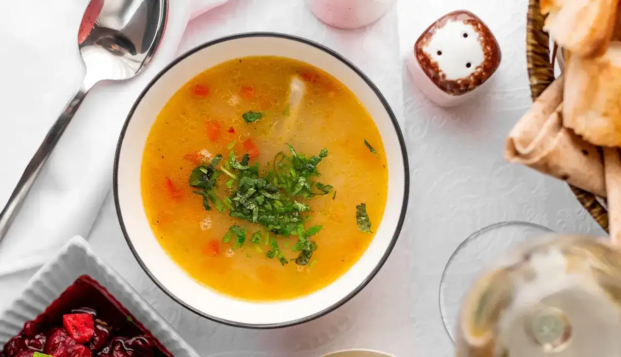 Aromatyczna zupa na rosole, z kawałkami warzyw i świeżą natką pietruszki, podana z pieczywem.