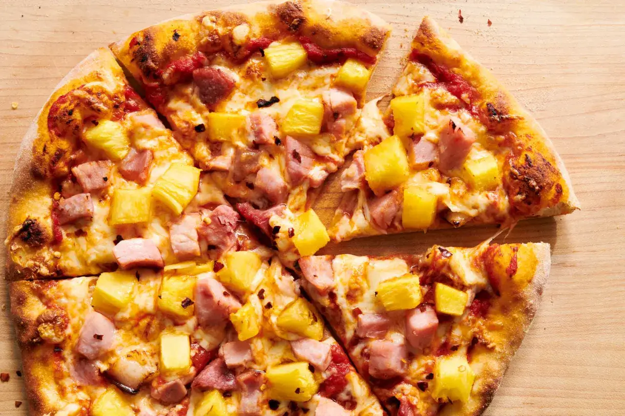 Gorąca pizza z ananasem i szynką, pokrojona na kawałki, z ciągnącym się serem.