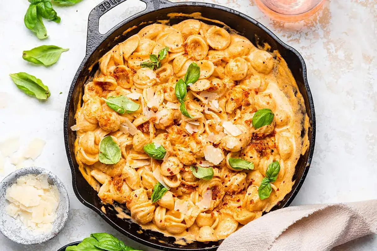 Orecchiette w kremowym sosie z suszonych pomidorów, posypane parmezanem i świeżą bazylią.