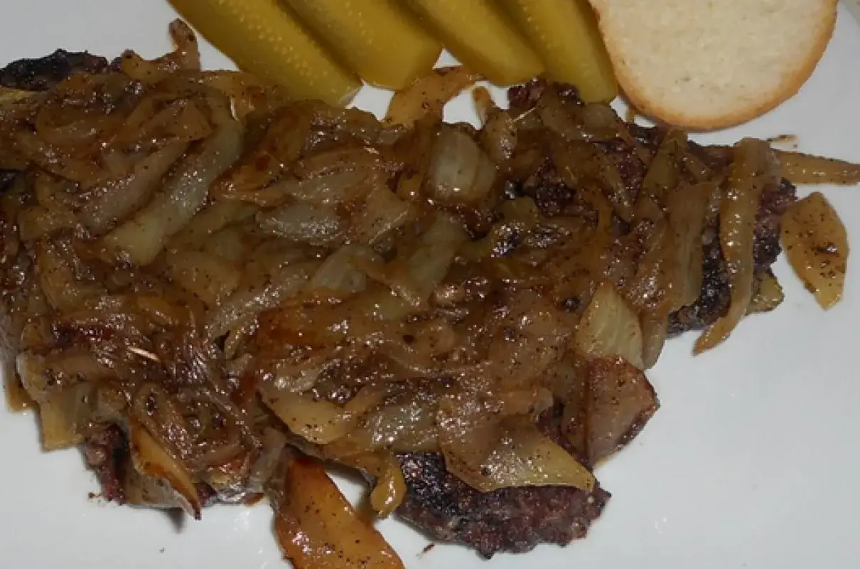 Pyszna kaszanka z cebulą, podana z ogórkami kiszonymi i kromką chleba.