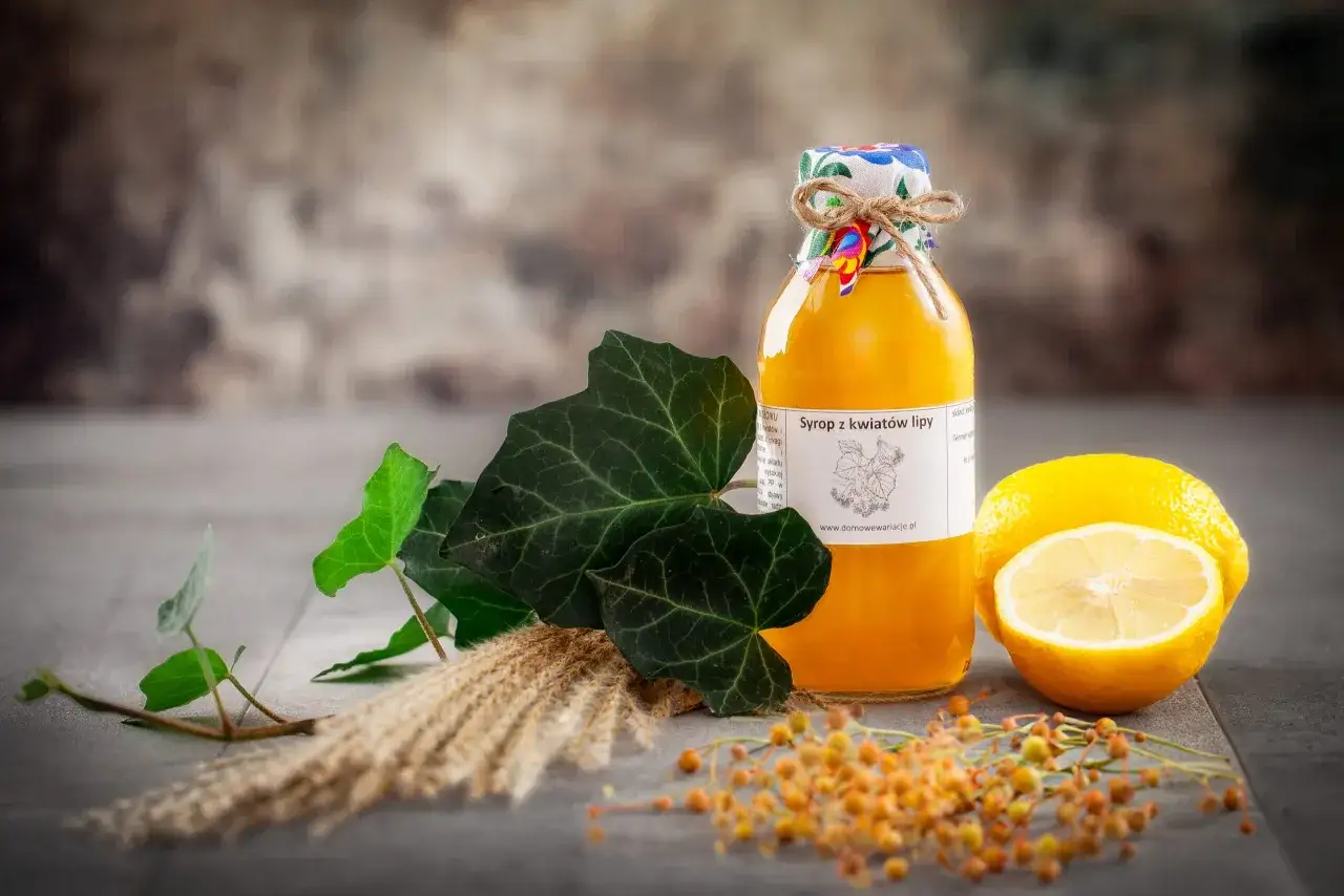 Złocisty syrop z kwiatów lipy w butelce, obok cytryny i zielonych liści. Naturalny, domowy produkt.