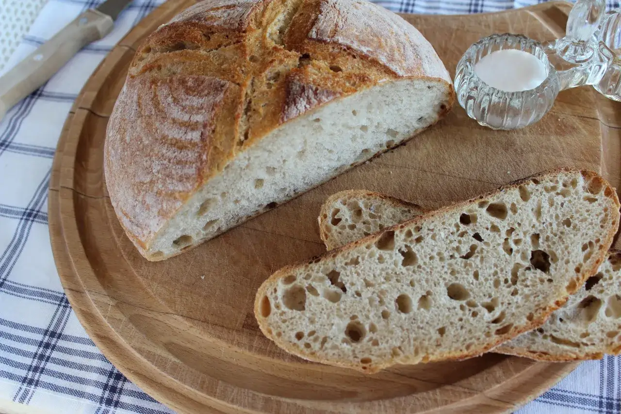 Chleb pszenno żytni na zakwasie, pokrojony na desce, z solniczką i nożem.