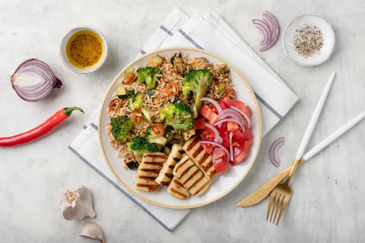 Pyszny ryż z warzywami i grillowany halloumi, podany z sałatką z pomidorów i cebuli. Idealny posiłek dla miłośników zdrowego jedzenia.