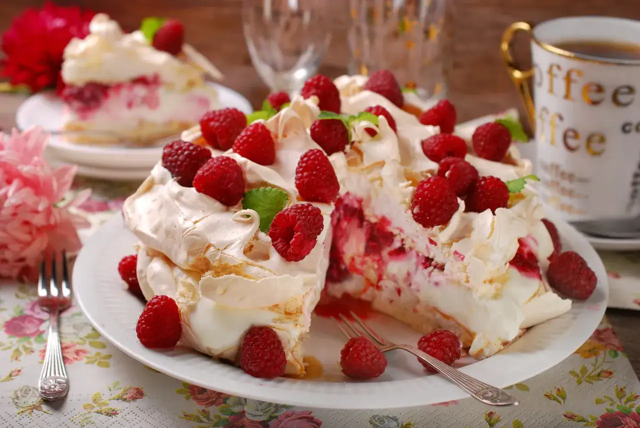 Pyszny tort bezowy z mascarpone i bitą śmietaną, udekorowany malinami i miętą. Idealny na deser!