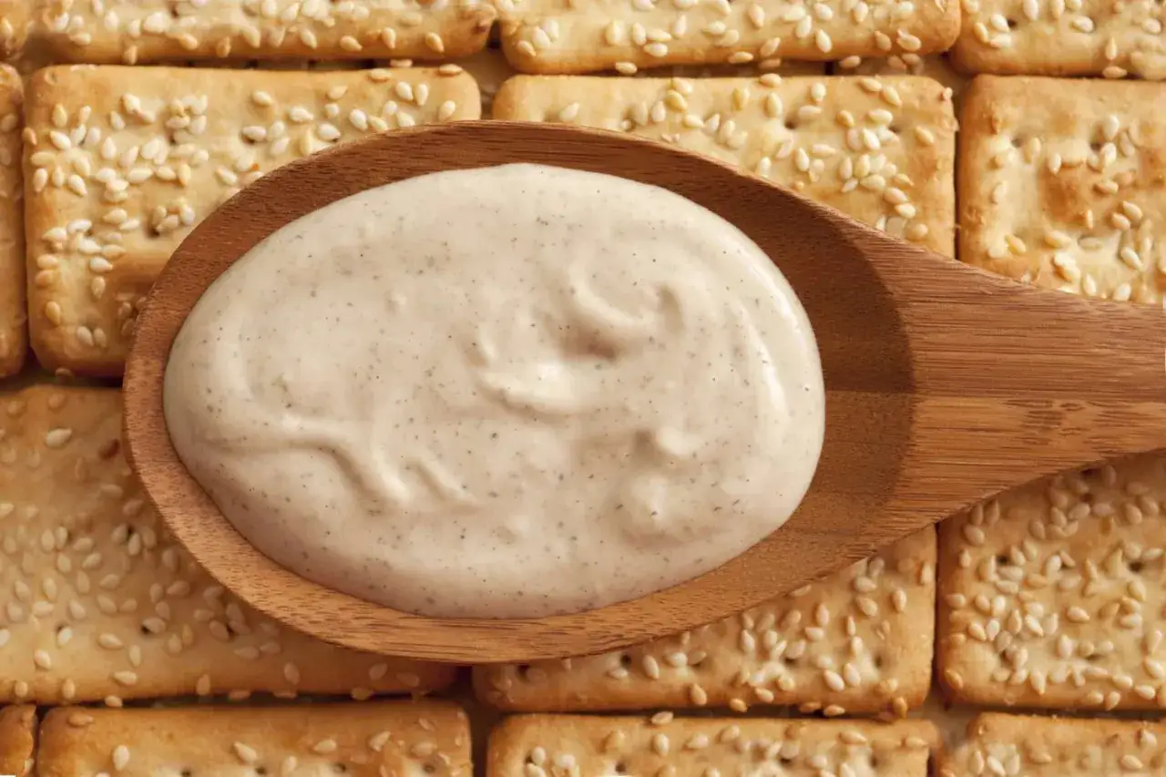 Kremowy sos na drewnianej łyżce, idealny do krakersów z sezamem. Czy to tahini? Co to jest tahini?