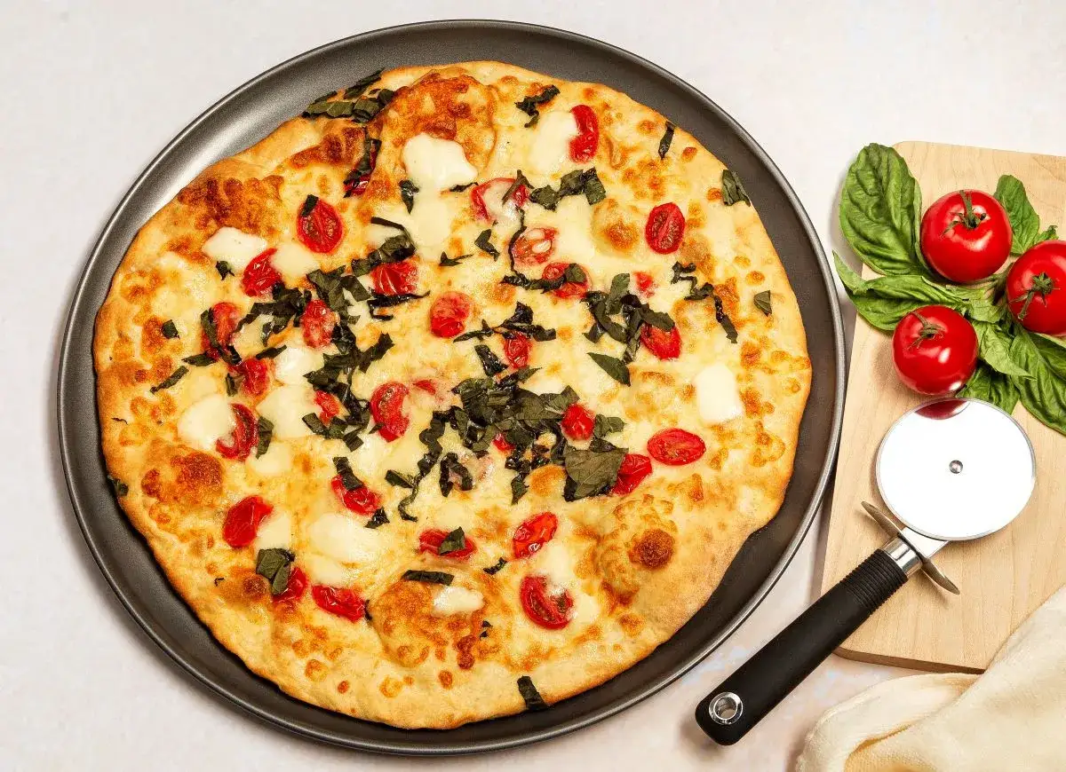 Pyszna pizza z serka wiejskiego, pomidorkami koktajlowymi i bazylią. Obok leżą świeże pomidory i nóż do pizzy.