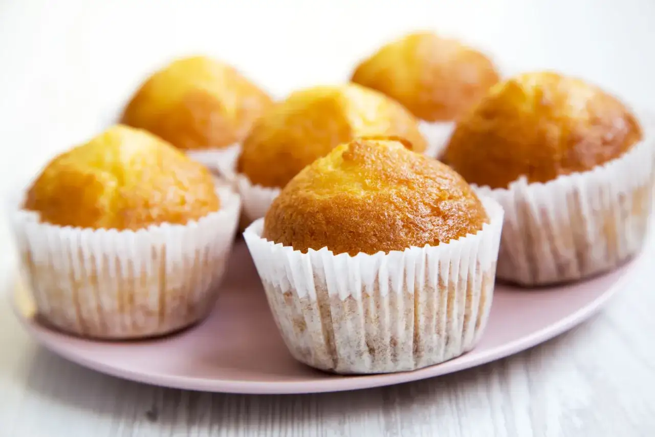 Idealny przepis na wilgotne i puszyste muffinki. Złociste, pachnące babeczki na różowym talerzyku.