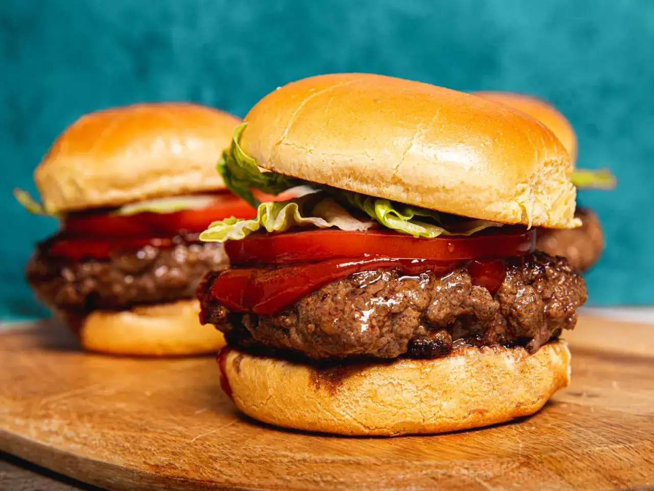 Dwa soczyste burgery z idealnie wysmażonym mięsem na burgera, bułką, pomidorem i sałatą.