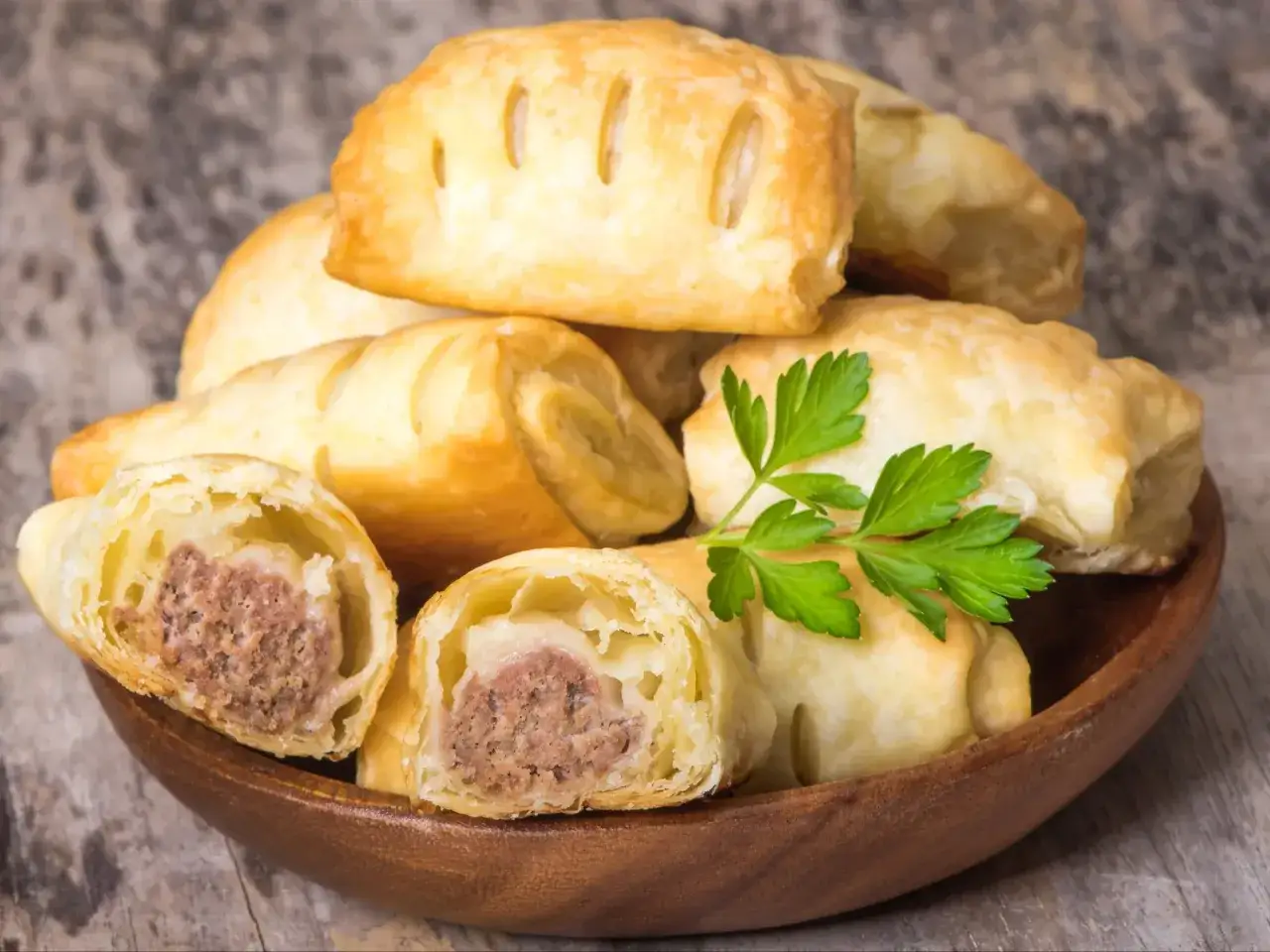Stos pieczonego ciasta francuskiego z mięsnym farszem, ozdobiony gałązką pietruszki.