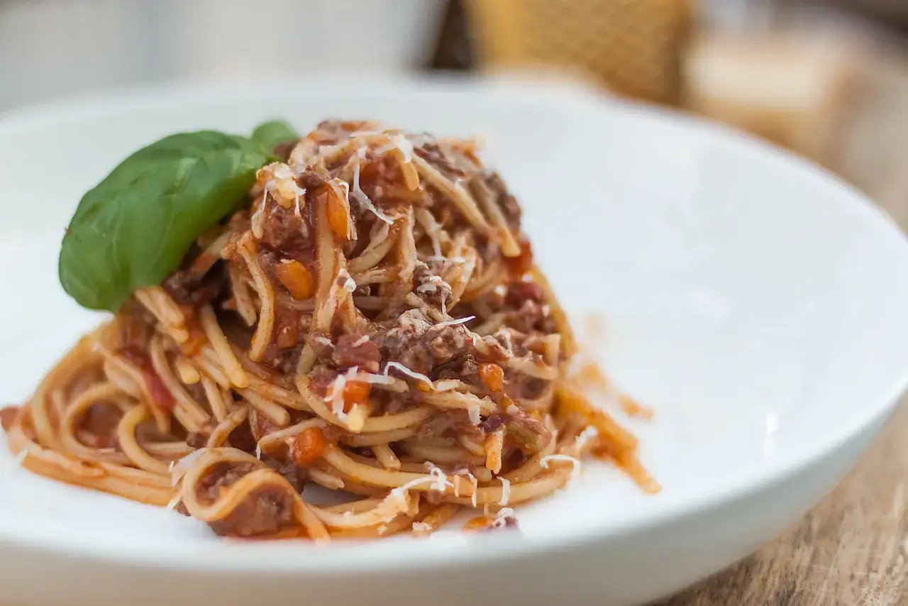 Pyszne spaghetti bolognese, przepis oryginalny, z aromatycznym sosem mięsnym, posypane parmezanem i ozdobione listkiem bazylii.