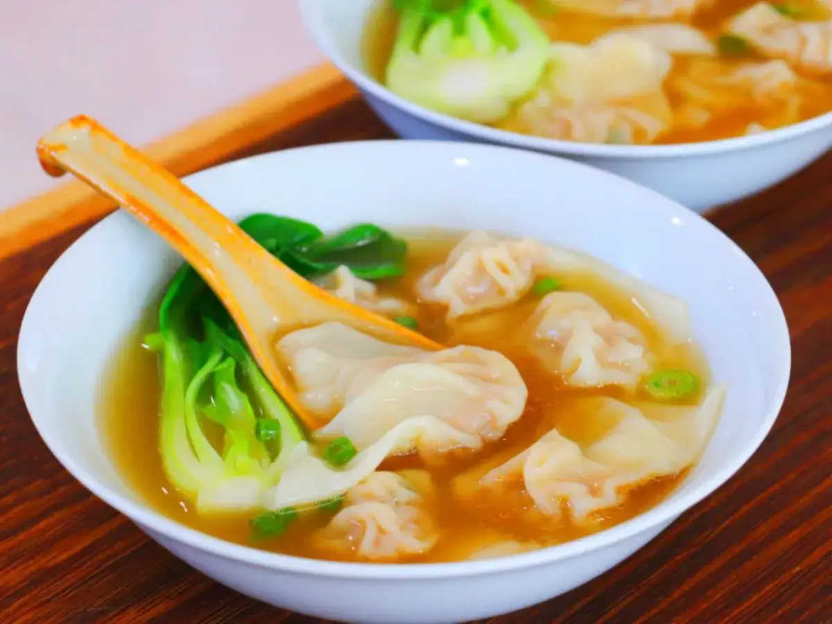 Aksamitna zupa wonton z zielonymi warzywami i pomarańczową łyżką. Pyszne pierożki unoszą się w aromatycznym bulionie.