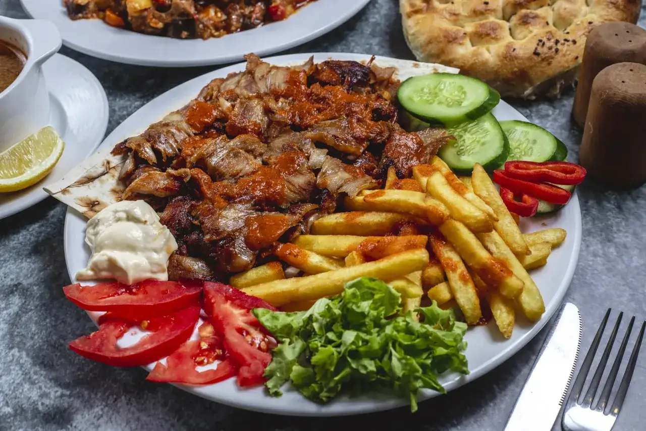 Talerz pełen mięsa gyros, frytek, warzyw i sosu. Prawdziwa uczta dla miłośników kuchni greckiej.