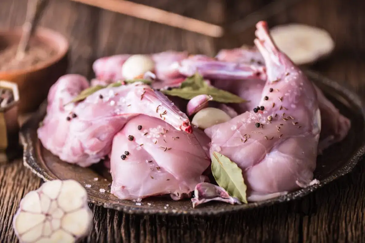 Surowe kawałki królika, przyprawione pieprzem, solą, kminkiem, liśćmi laurowymi i czosnkiem, gotowe do pieczenia. Idealna marynata do królika pieczonego w piekarniku.