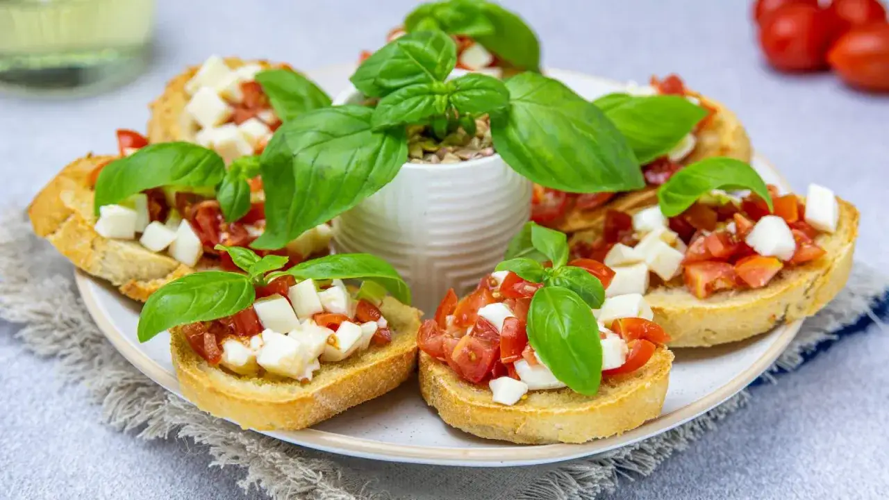 Bruschetta z pomidorami i mozzarellą – pyszny przepis na letnią przekąskę. Chrupiące grzanki z soczystymi pomidorami i kremową mozzarellą, ozdobione świeżą bazylią.